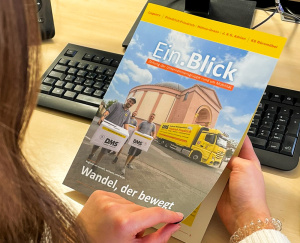 Eine Frau liest am Schreibtisch die Unternehmenszeitschrift „Ein.Blick“ (2025/02)