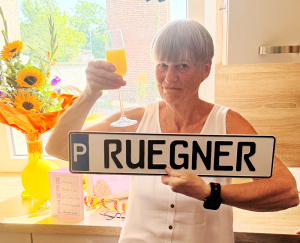 Elke Rügner mit einem Sekt-Glas und ihrem Parkschild in den Händen